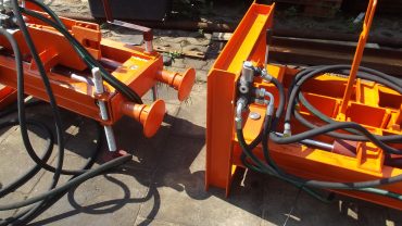 Pomarańczowe urządzenie hydrauliczne z przewodami i metalowymi wspornikami na utwardzonym podłożu.